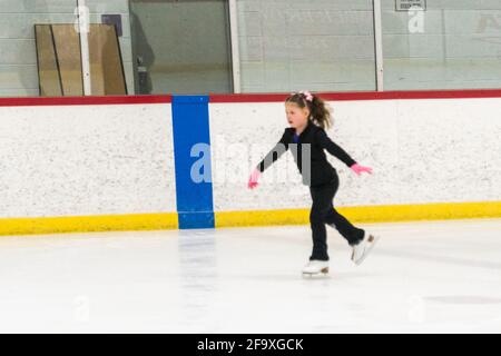 Kleine Mädchen, die Eiskunstlauf üben, bewegen sich auf der Indoor-Eisbahn. Stockfoto