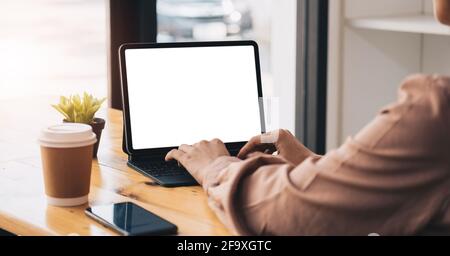 Kurze Aufnahme einer jungen professionellen Geschäftsfrau, die auf einem leeren Tablet und Büromaterial am einfachen Arbeitsplatz tippt. Stockfoto