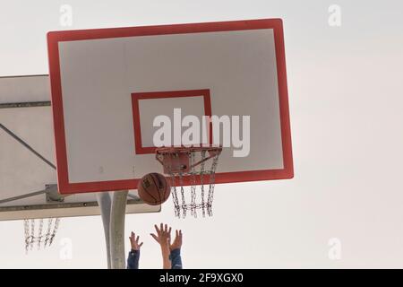 Ein Basketball, der an einem Frühlingsnachmittag in der Luft über den greifenden Händen der Spieler unter dem Reifen und dem Backboard in einem Nachbarschaftspark eingefroren wurde. Stockfoto