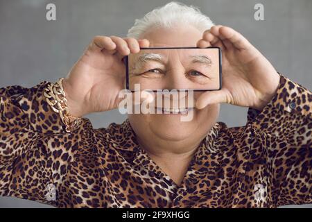 Lustige reiche mollige ältere Mann in einem Leoparden-Hemd mit Spaß mit seinem Handy Stockfoto
