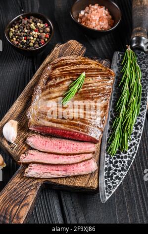 BBQ gegrillte Flanke oder Lasche Rindersteak auf einem hölzernen Schneidebrett. Schwarzer Holzhintergrund. Draufsicht Stockfoto