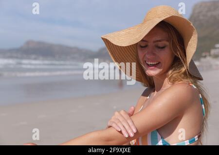 Kaukasische Frau trägt einen Bikini, sitzt auf einem Handtuch und setzt Sonnencreme an Am Strand Stockfoto