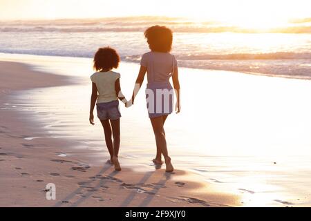 afroamerikanische Mutter und Tochter gehen und halten sich die Hände an Der Strand Stockfoto