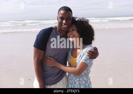 afroamerikanisches Paar steht und umarmt am Strand lächelnd Stockfoto