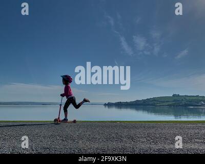 Junges Mädchen auf einem Roller mit Appledore im Hintergrund, Devon, Großbritannien Stockfoto