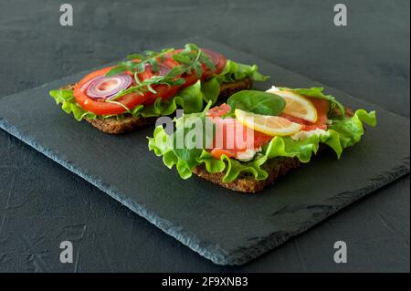 Gemüse und geräucherte offene Sandwiches mit Quark, Gitter, Tomaten und Zitrone auf einem Schiefer. Gesundes Frühstück für die Ernährung. Stockfoto