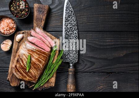 BBQ gegrillte Flanke oder Klappe Rindfleisch Steak auf einem Holzschneidebrett. Schwarzer Holzhintergrund. Draufsicht. Speicherplatz kopieren Stockfoto