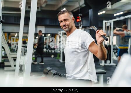 Attraktiver, selbstbewusster, gesunder Sportmann mit sitzender Lat-Pulldown-Maschine Im Fitnessstudio Stockfoto