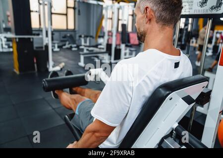 Attraktiver, selbstbewusster, gesunder Sportmann mit sitzender Beincurl-Maschine im Fitnessstudio, Seitenansicht Stockfoto