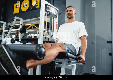 Attraktiver selbstbewusster gesunder Sportmann mit sitzender Beincurl-Maschine Im Fitnessstudio Stockfoto