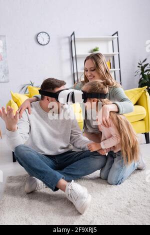 Vater und Tochter spielen mit vr-Headsets in der Nähe von positiver Mutter Auf dem Teppich Stockfoto