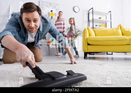 Lächelnder Mann, der Teppich mit Staubsauger putzt Stockfoto