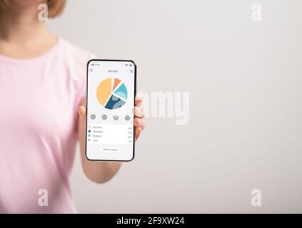 Nicht erkennbare Frau hält Smartphone mit Grafiken und Diagrammen auf dem Bildschirm Stockfoto