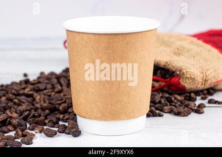 Einwegbecher aus braunem Karton mit Kaffee und gerösteten Kaffeebohnen auf dem Tisch mit Platz zum Kopieren auf hellem Hintergrund. Konzept für Essen zum Mitnehmen. Stockfoto