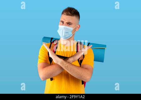 Reiseverbot während des Coronavirus. Serious Kerl mit Camping-Ausrüstung trägt Gesichtsmaske und gestikulierende STOP über blauen Hintergrund Stockfoto