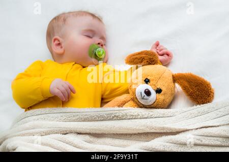 Nahaufnahme eines schlafenden Babys in einer Umarmung mit einem Spielzeug und einem Schnuller im Mund. Stockfoto