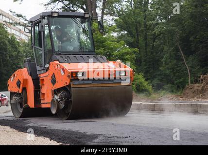 Große orange Walze in den Prozess des Rollens von heißem Asphalt. Pflasterarbeiten. Verbesserung der Stadt. Ausrüstung für Straßenbau und Reparatur Stockfoto