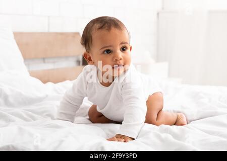 Afrikanisches Kleines Baby Kriecht Auf Dem Bett Und Schaut Im Schlafzimmer Zur Seite Stockfoto