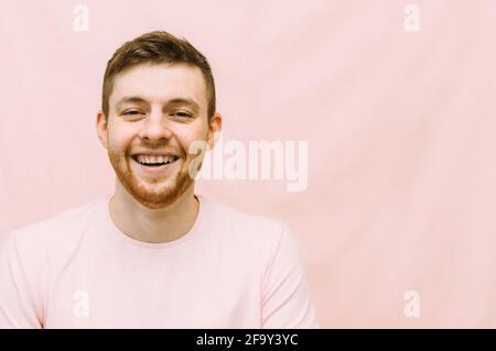 Der Mann lächelt in einem rosa T-Shirt auf einem rosa Hintergrund. Optimismus, Glückskonzept. Stockfoto