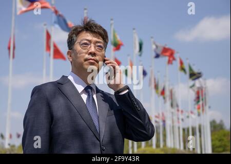 Ein asiatischer Geschäftsmann mittleren Alters, der ein Smartphone unter verschiedenen Nationalflaggen benutzt, die im Wind flattern. Stockfoto