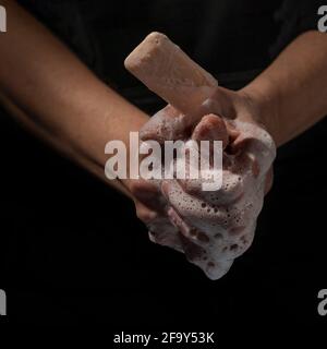Ein Stück Seife springt aus dem Schaumstoff einer Frau Hände auf dunklem Hintergrund Stockfoto