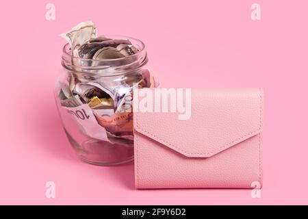 Euro- und Dollar-Banknoten im Glas-Geldglas mit leerem Etikett und rosa Brieftasche, finanziell, sparend. Spardose mit leerem Haftnotizpapier. Glas voll mit C Stockfoto