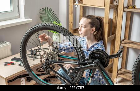 Eine Frau führt Wartungsarbeiten an seinem Mountainbike durch. Konzept der Befestigung und Vorbereitung des Fahrrads für die neue Saison Stockfoto