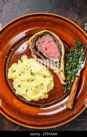 Beef Wellington Gebäck mit Kartoffelbrei auf einem rustikalen Teller. Dunkler Hintergrund. Draufsicht Stockfoto