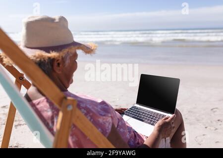 Ältere afroamerikanische Frau mit Laptop, während sie auf Deck sitzt Liege am Strand Stockfoto