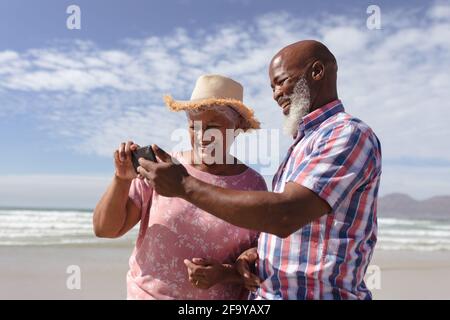 Glückliches afroamerikanisches Senioren-Paar mit Smartphone am Strand Stockfoto