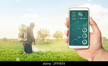 Eine Hand mit einem Telefon auf dem Hintergrund eines Landwirts mit landwirtschaftlicher Rauchnebelsprühmaschine. Kontrolle der Verwendung von Chemikalien, die Lebensmittel anbauen. Pflanzenpflege A Stockfoto