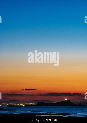 Silhouette von Fidra Island mit Licht vom Leuchtturm bei Sonnenuntergang mit einem bunten Himmel, Firth of Forth, Schottland, Großbritannien Stockfoto