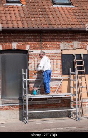 Sint Gillis Waas, Belgien, 21. April 2021, älterer Handwerker, der als Maler arbeitet, bereitet die Wand eines Hauses für die Malerei vor Stockfoto