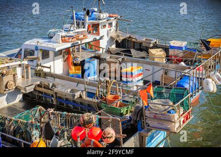 Drei kleine Fischerboote mit Ausrüstung beladen. Seile verankern sie am Ufer und ihre Reflexionen liegen im Wasser. Stockfoto