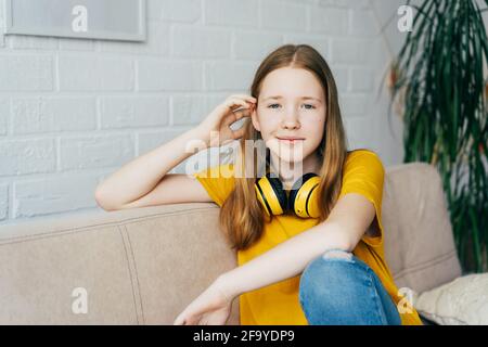 Porträt eines rothaarigen blauäugigen Teenagers mit kabellosen Kopfhörern zu Hause auf der Couch. Stockfoto