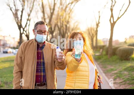 Älteres Paar, das während der Gehzeit eine Schutzmaske mit hydroalkoholischem Gel für die Handreinigung trägt. Konzept der Pflege und Maßnahmen zum Schutz der o Stockfoto