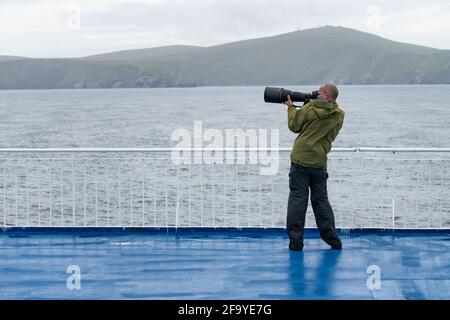 Hirsthals, Dänemark - 05.20.2017: Ein männlicher Fotograf mit großem Teleobjektiv macht ein Foto auf dem Deck eines Kreuzschiffs auf dem Weg nach Island. Stockfoto