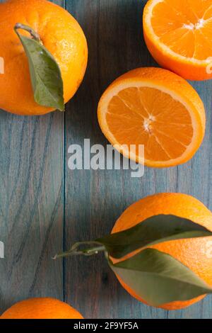 Orange in zwei Hälften geschnitten und andere Orangen auf ultramarinfarben gefärbt Holzhintergrund Stockfoto