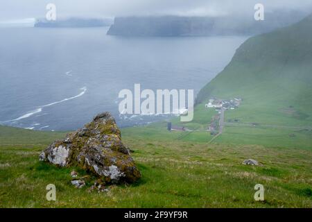 Das faroesische Dorf Trollanes von einem Hügel aus gesehen. Grüne Hügel, trübes, nebliges Wetter im wilden Norden. Eher ruhiges Meer und typisch kleines Hous Stockfoto