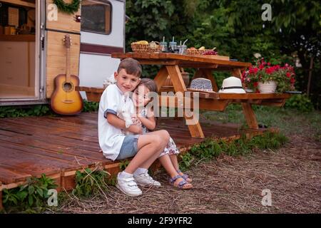 Junge und Mädchen sitzen auf dem Holzboden auf dem Lastwagen und halten einen flauschigen Kaninchenhase in den Händen. Bruder Schwester umarmen, spielen mit inländischen har Stockfoto