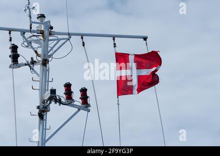 Dänische Flagge winkt im Wind mit bewölktem Himmel im Hintergrund. Am Fahnendraht auf einem Kreuzschiff befestigt. Stockfoto