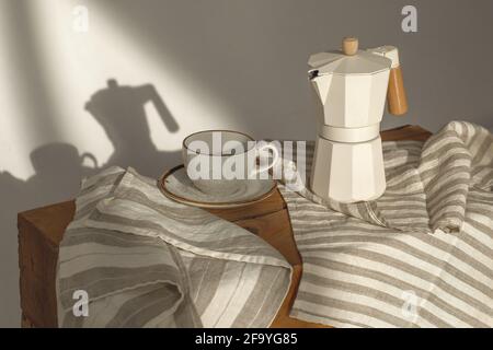Italienische Kaffeemaschine mit Holzgriff und weißem Kaffee tasse auf Massivholz-Stempel mit Geschirrtüchern in dekoriert Cremige Töne auf Sonnenlicht schaffen Stockfoto