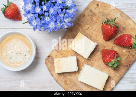 Reife, rote Erdbeeren, Stück Kuchen mit Quark, Kaffee, Schneeglöckchen Blumen auf dem Tisch. Oberes Layout. Stockfoto