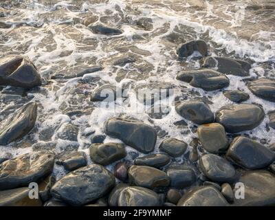 Das Meer spült sich gegen nasse Kieselsteine an der Küste. Stockfoto