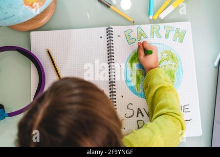 Draufsicht auf Kindermädchen zeichnet die Erde mit Wachs Farben auf Schulnotizbuch für den Tag der Erde - wenig Aktivist Mädchen schreibt die Botschaft Save the Planet - Stockfoto