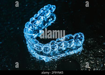 Transparente Ausrichter, Zahnhalter liegen auf Glas mit Wassertropfen auf schwarzem Hintergrund Stockfoto