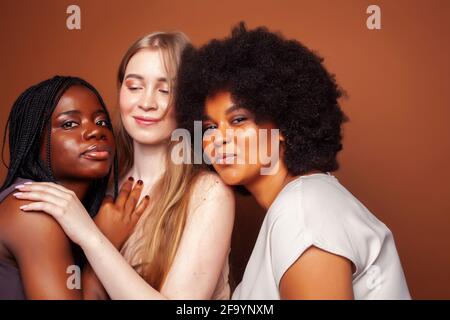 Junge hübsche kaukasische, afro, skandinavische Frau posiert fröhlich zusammen auf braunem Hintergrund, Lifestyle diverse Nationalität Menschen Konzept Stockfoto