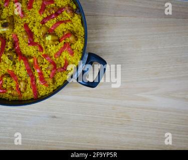 Traditionelle spanische Paella mit Meeresfrüchten, Schweinswürsten, Schweinerippchen und roten Paprika in einer Pfanne auf einem Holztisch und einer Serviette Stockfoto