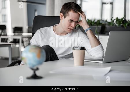 Beunruhigt Student Blick auf Laptop in der Nähe von Papierbecher auf dem Schreibtisch Stockfoto