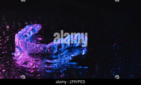 Transparente Ausrichter, Zahnhalter liegen auf Glas mit Wassertropfen auf schwarzem Hintergrund Stockfoto